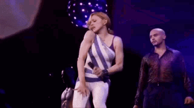 a woman is dancing on a stage in front of a microphone while a man stands behind her .