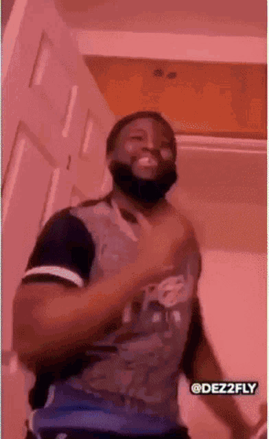 a man with a beard is dancing in a room with a pink light behind him .