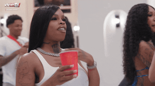 a woman in a white tank top holds a red cup in her right hand