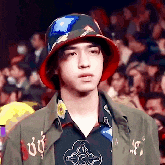 a young man wearing a bucket hat and a green jacket is standing in front of a crowd .