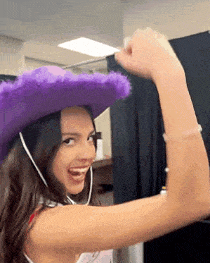 a young woman wearing a purple cowboy hat is flexing her muscles .