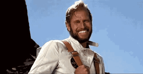 a man with a beard wearing suspenders and a white shirt smiles