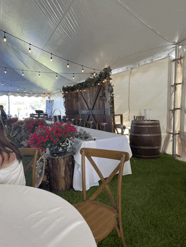 a white tent with tables and chairs and barrels in the grass