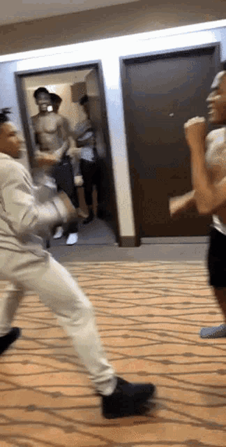 two men are fighting in a hallway while a shirtless man stands behind them