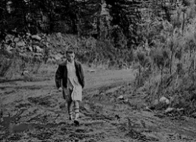 a black and white photo of a boy walking down a muddy road .