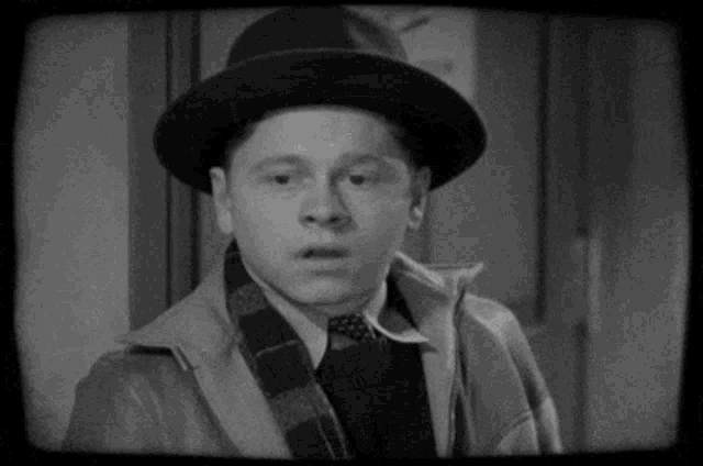 a black and white photo of a man wearing a hat , scarf , jacket and tie .