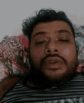 a man with a beard and curly hair is laying on a bed with his eyes closed .