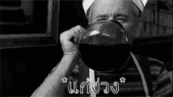 a black and white photo of a man drinking from a large bowl .