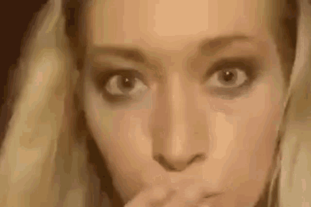 a close up of a woman covering her mouth with her hand and looking at the camera .