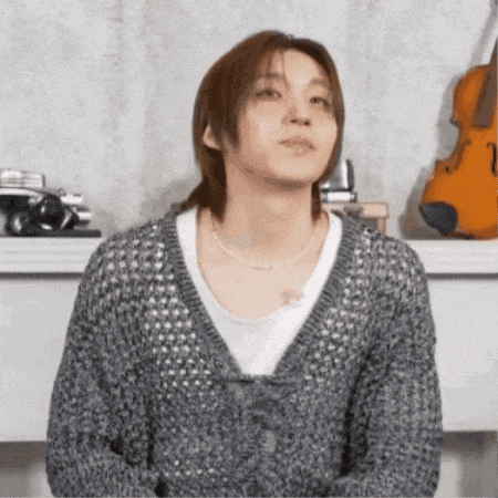 a man wearing a grey sweater and a white shirt is standing in front of a violin .