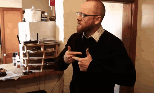 a man wearing glasses and a black sweater is pointing at something