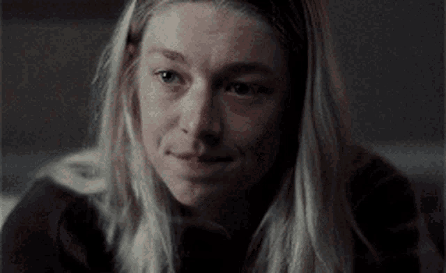 a woman with long blonde hair is smiling in a dark room .