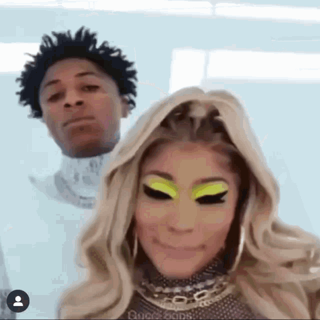 a man and a woman are posing for a picture together . the woman is wearing a wig and green eye shadow .