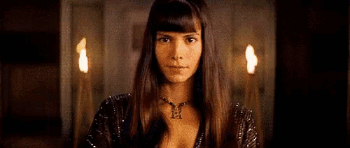 a woman with long hair and a necklace is standing in front of a candle in a dark room .