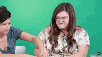 two women are sitting at a table with a green background and one of them is holding the other 's arm