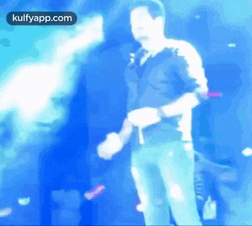 a man in a blue shirt is dancing on a stage with the words kulfyapp.com on the bottom