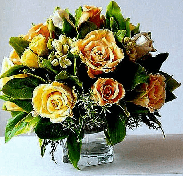 a vase filled with yellow roses and green leaves is sitting on a table .