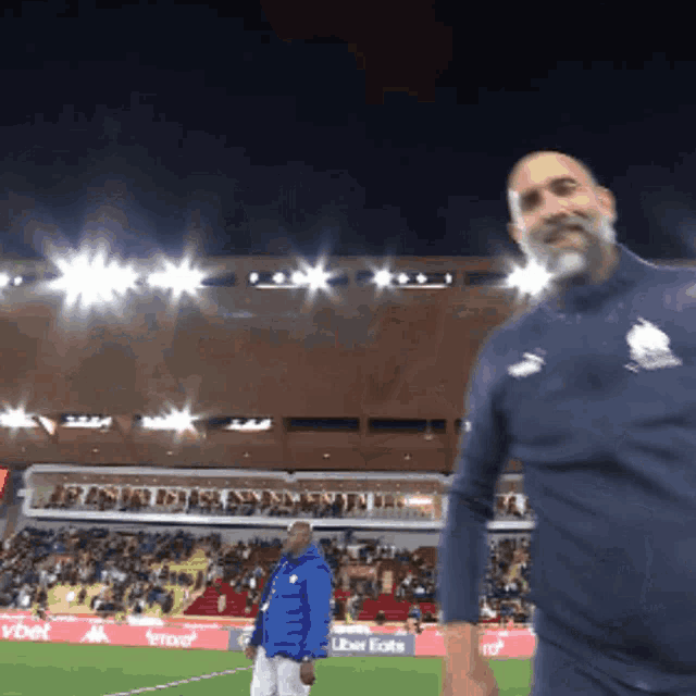 a man in a blue jacket stands on a soccer field in front of an uber eats advertisement
