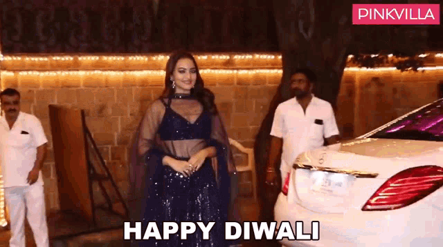 a woman in a blue dress is standing in front of a white car that says happy diwali on it