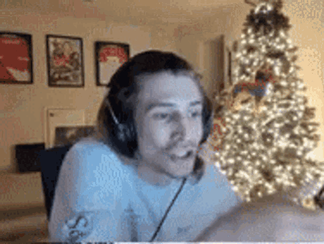 a man wearing headphones and a white shirt is sitting in front of a christmas tree .