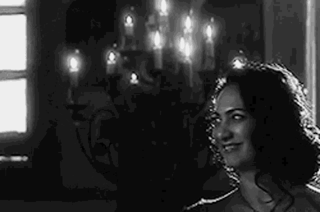 a woman is smiling in a black and white photo while standing in front of a chandelier .