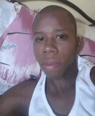 a bald man in a white tank top is taking a selfie in bed .