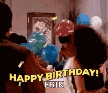 a group of people are standing in a room with balloons and confetti and a woman is saying `` happy birthday erik '' .
