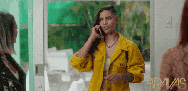 a woman in a yellow jacket is talking on a cell phone with bravas written on the bottom