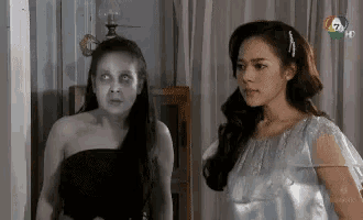 two women are standing next to each other in a room . one of the women is a ghost with glowing eyes .