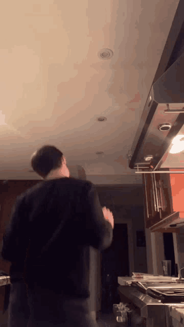 a man in a black shirt is standing in a kitchen with a stove top oven