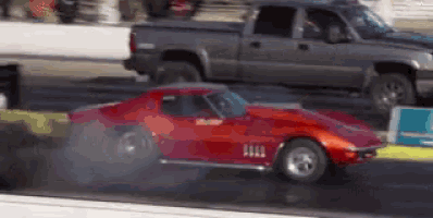 a red corvette is driving down a race track with smoke coming out of its tires