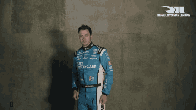 a man in a blue and white racing suit with the number 15 on it gives a thumbs up
