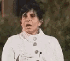 a woman wearing a white sweater and a white coat is making a funny face .