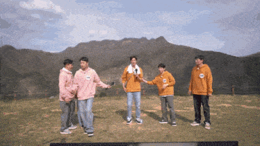 a group of men are standing in a field with one wearing a pink sweatshirt with the letter k on the front