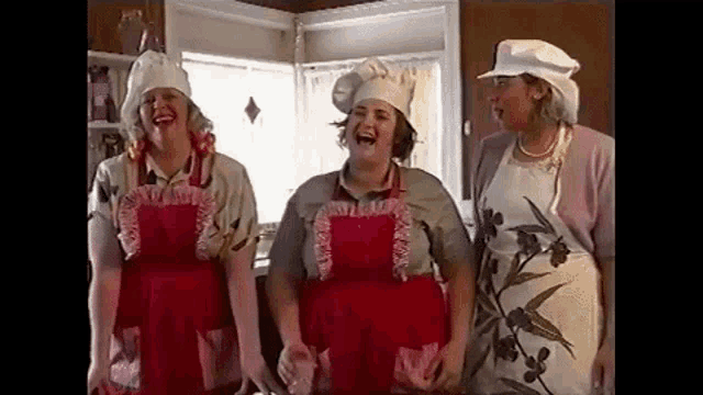 three women wearing chef hats and aprons are standing next to each other in a kitchen .