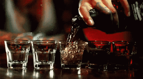 a person is pouring a drink into four shot glasses on a table .