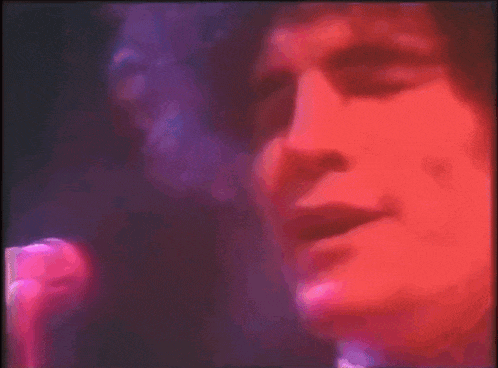 a close up of a person singing into a microphone with a pink and purple background .