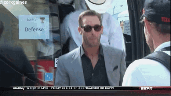 a man in a suit and sunglasses stands in front of a sign that says defense
