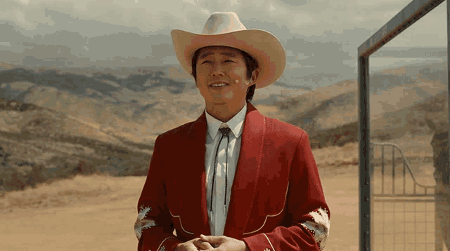 a man in a red jacket and cowboy hat smiles