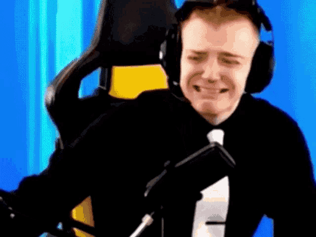 a man wearing headphones and a tie is sitting in a chair and talking into a microphone .