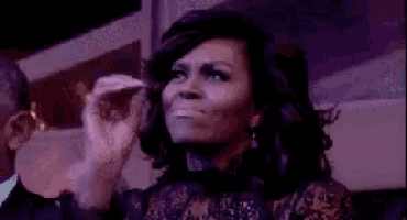 michelle obama is making a funny face while sitting in a dark room .