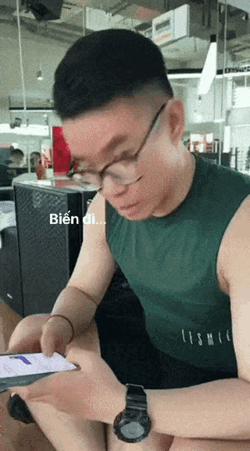 a man wearing glasses and a green shirt is looking at a phone