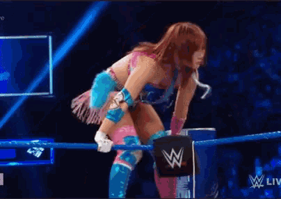 a female wrestler is standing in a ring with a w logo in the background