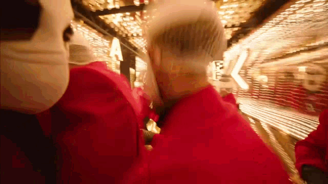 a blurry picture of a group of people in red jackets and masks walking down a staircase .