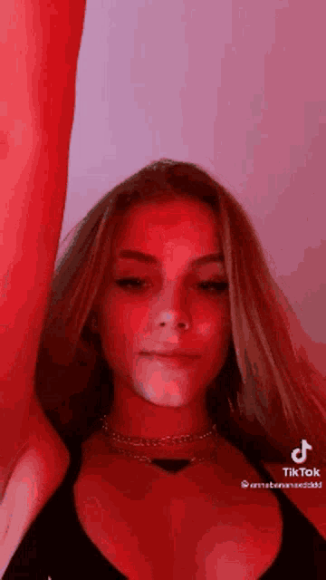 a woman in a black tank top is standing in front of a red wall .