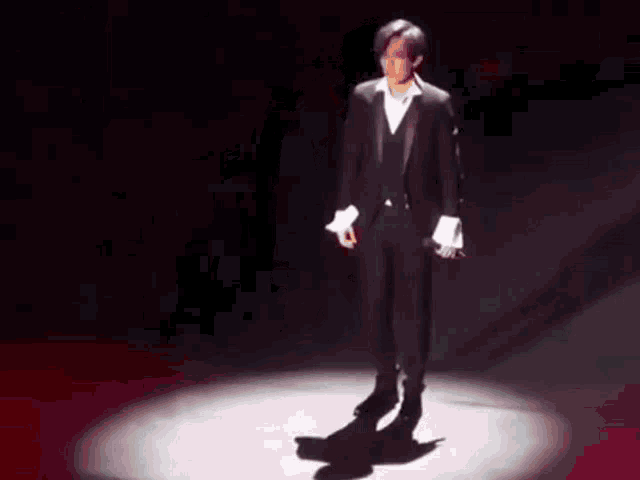 a man in a tuxedo is standing in front of a spotlight on a stage .