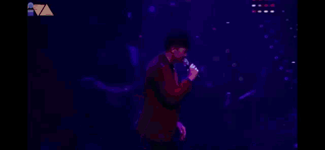 a man in a red jacket singing into a microphone on stage