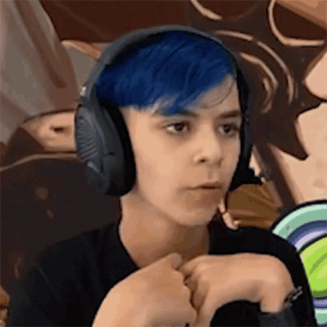 a young boy with blue hair is wearing headphones and looking at the camera .
