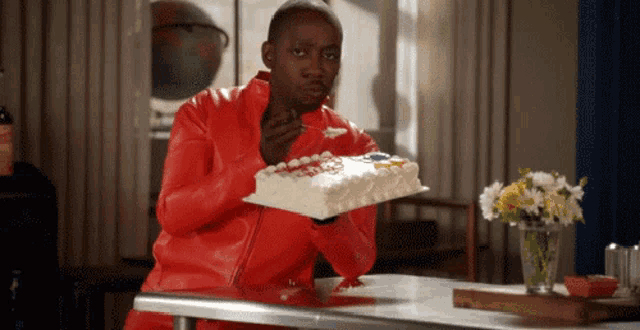 a man in a red jacket is sitting at a table holding a cake