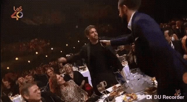a man in a suit is dancing in front of a crowd of people at a party .